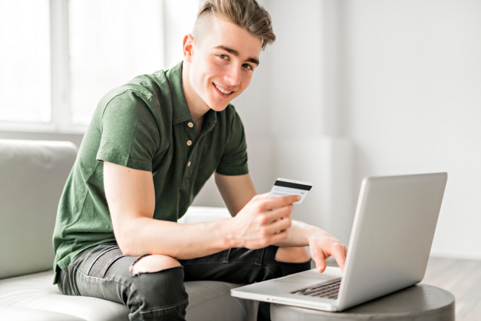 Teen boy holding a credit card using a laptop